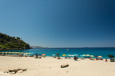 Group of people at beach against clear blue sky during sunny day