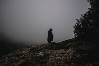 Low angle view of silhouette man standing on rock against sky