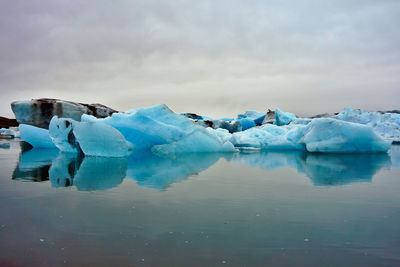 Icebergs in lake against cloudy sky
