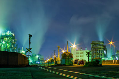 Illuminated street amidst factory against sky at night