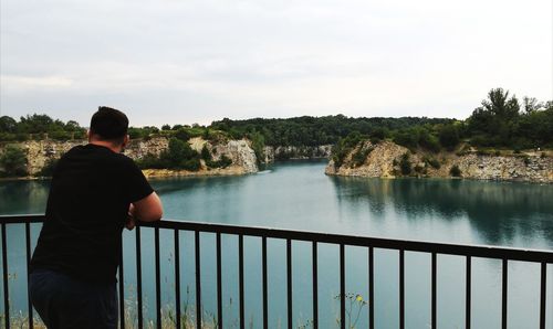 Rear view of man standing by railing against sky