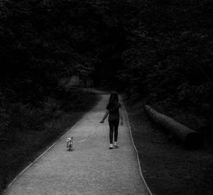 Rear view of girl walking with dog on road