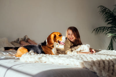Smiling girl sitting by dog on bed at home