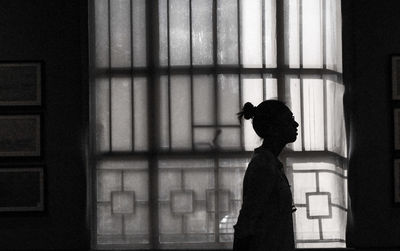 Side view of silhouette woman standing against window