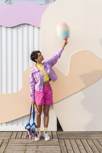 Smiling woman with roller skates holding cotton candy in front of wall