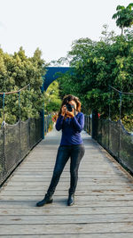 Full length of woman photographing on footbridge