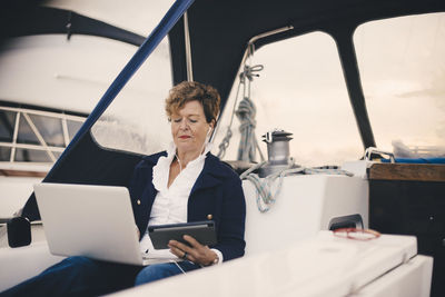 Senior woman using digital tablet and laptop in yacht