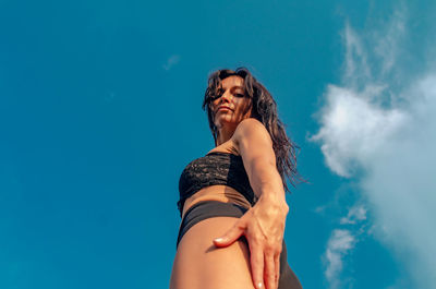 Low angle portrait of woman standing against blue sky
