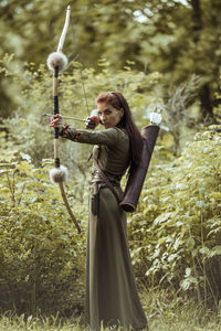 Beautiful archer holding bow and arrow standing against trees