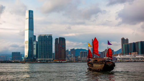 Sailboats in river by modern buildings against sky