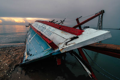 Low angle view of abandoned ship on beach against sky