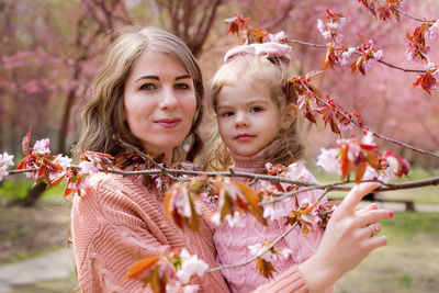 Portrait of mother and daughter in the park with blooming pink sakura