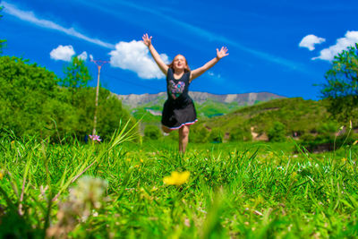 Surface level of girl with arms raised running on land against blue sky