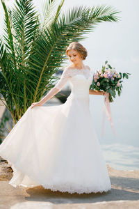 Woman with bouquet standing by palm tree