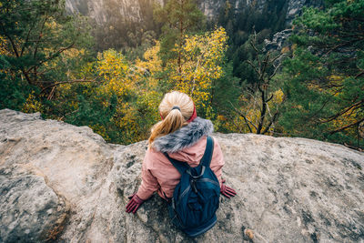 Rear view of woman sitting on rock while looking at view