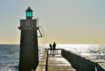 Rear view of man walking on pier over sea against sky during sunset