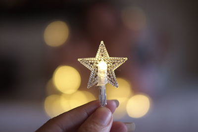 Cropped hand holding illuminated christmas light at night