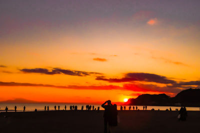 Silhouette people at beach against sky during sunset