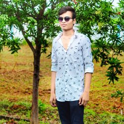 Portrait of young woman wearing sunglasses standing against trees