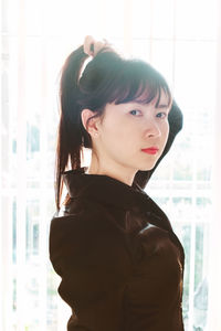 Portrait of young woman looking away while standing against window