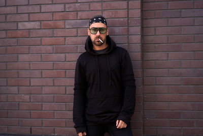 Portrait of young man with cigarette while standing against brick wall