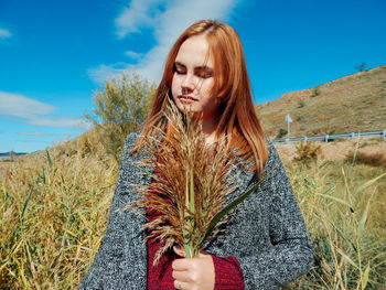 Young woman with eyes closed holding leaves while standing on land against sky