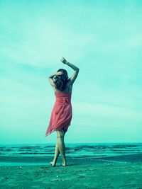 Rear view of woman standing at beach against cloudy sky