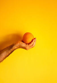 Orange in hand on yellow wall