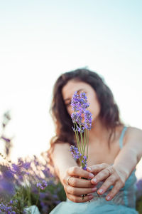 Midsection of woman holding purple flowering plant against sky