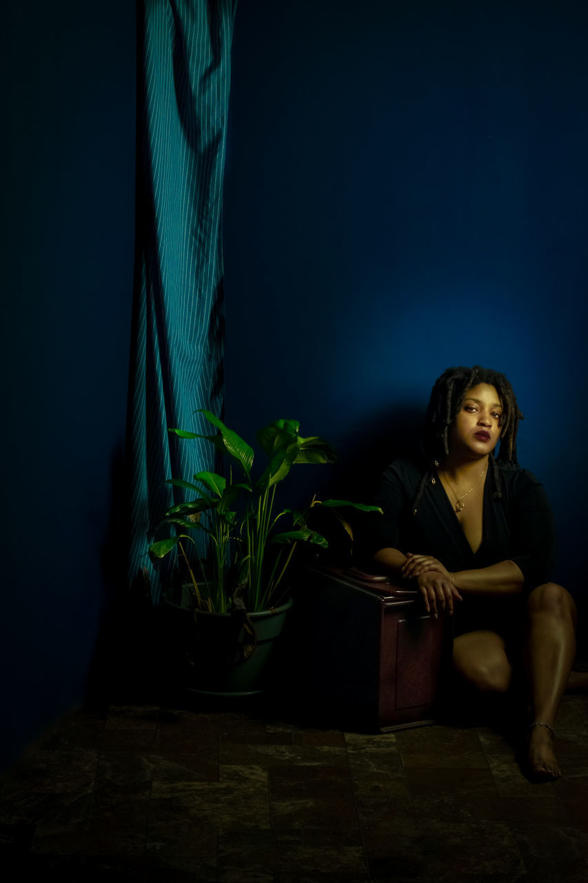 darkness, one person, adult, light, women, sitting, indoors, young adult, dark, full length, night, plant, looking, blue, screenshot, emotion, nature, lifestyles, person, female, portrait, contemplation, copy space, loneliness, hairstyle, relaxation, potted plant