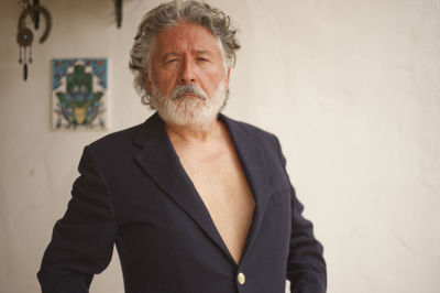 Portrait of senior man wearing blazer standing against wall at home