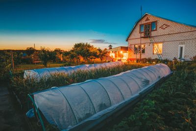 Illuminated house by building against sky at sunset