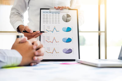 Midsection of businessman explaining graph to colleague at desk