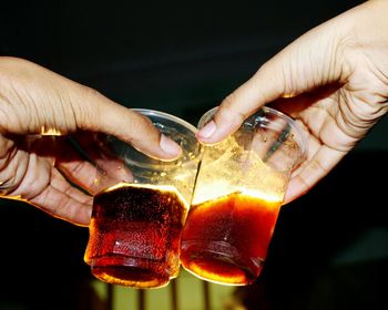 Cropped hands toasting drinks against sky at night