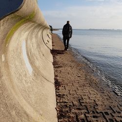 Rear view of man standing on beach against sky leading line