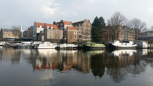 Sailboats moored in canal by buildings in city against sky
