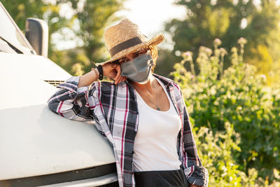 Woman wearing mask and hat standing by car