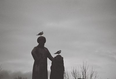 Silhouette of birds perching on statue against sky