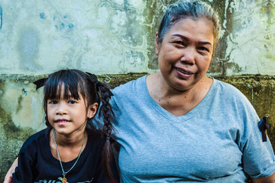 Portrait of mother and daughter sitting against weathered wall