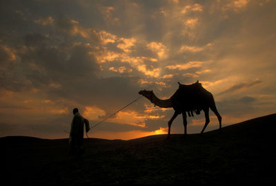 Silhouette woman standing on field against sky during sunset