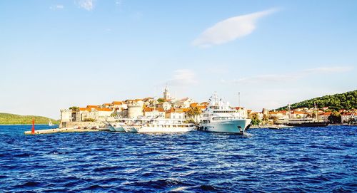 Boats in calm sea in front of harbor against sky