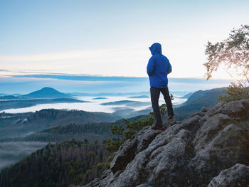 Hiking in sunrise. man hiker wear hood and blue windcheater stay alone in sunset at mountain edge