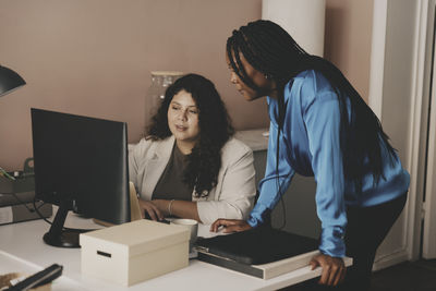 Multiracial female business colleagues discussing over computer at desk in office