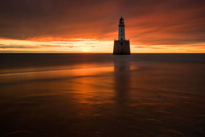 Lighthouse by sea against sky during sunset