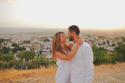 Young couple looking each other face to face while standing in city at sunset