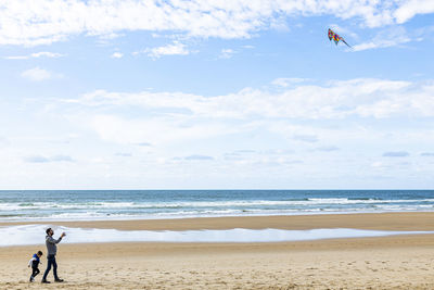 People playing with kite at beach against sky