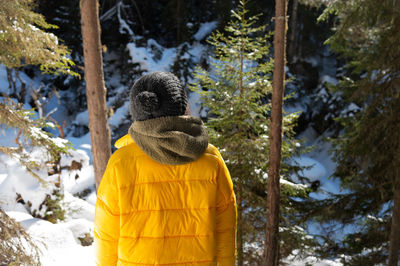 Snowy weather in a coniferous forest, a girl standing behind in winter, in a gray knitted hat 