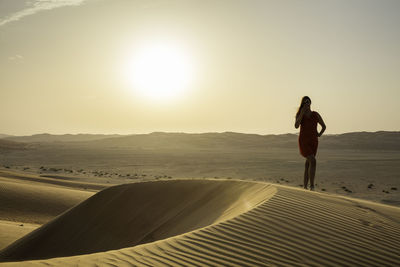 Woman standing at desert against clear sky