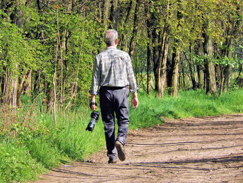 Rear view of man with dslr camera walking on footpath in forest