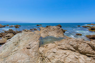 Rocks on beach against clear blue sky